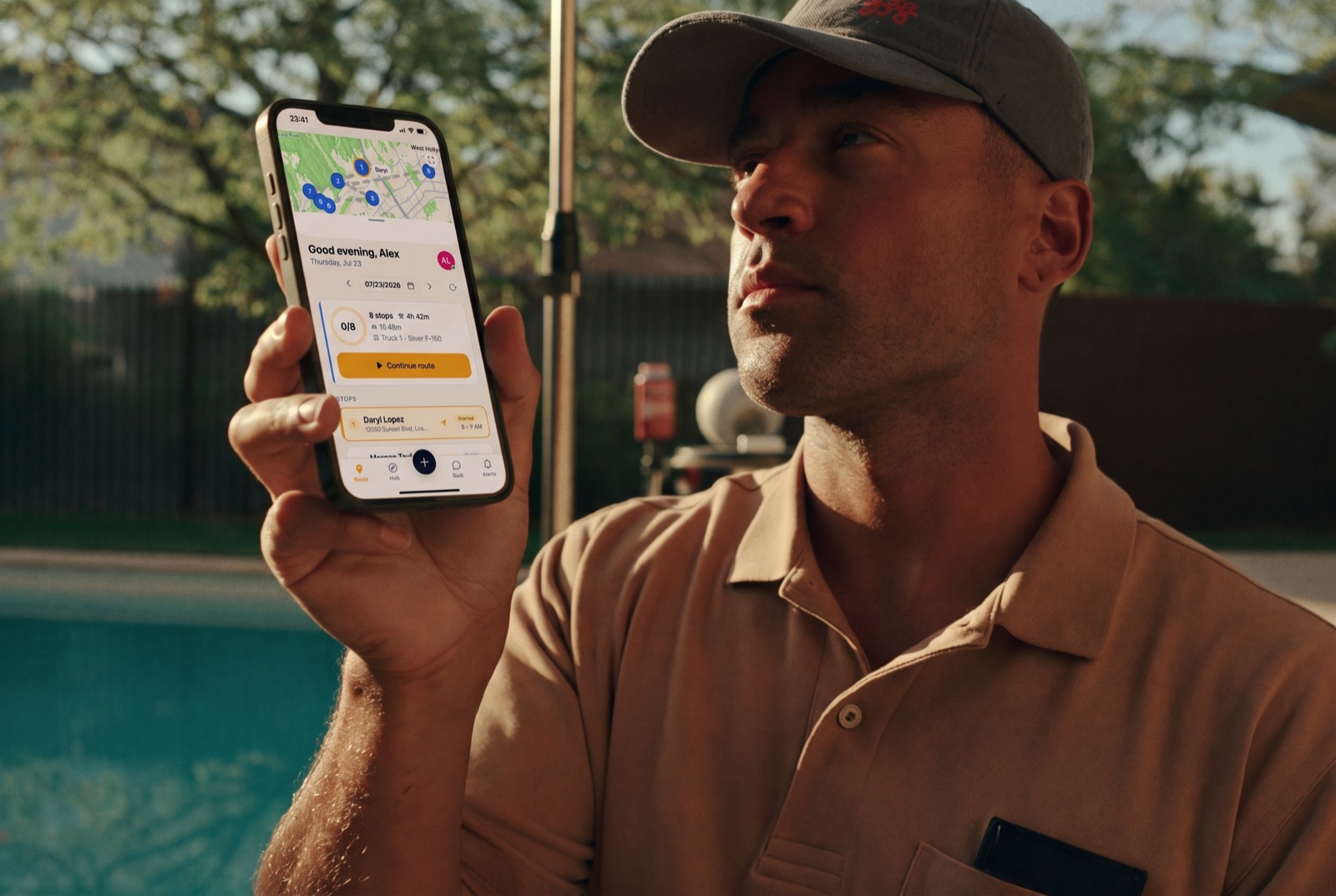 Pool technician in a cap checking today's route on their phone at a customer's poolside